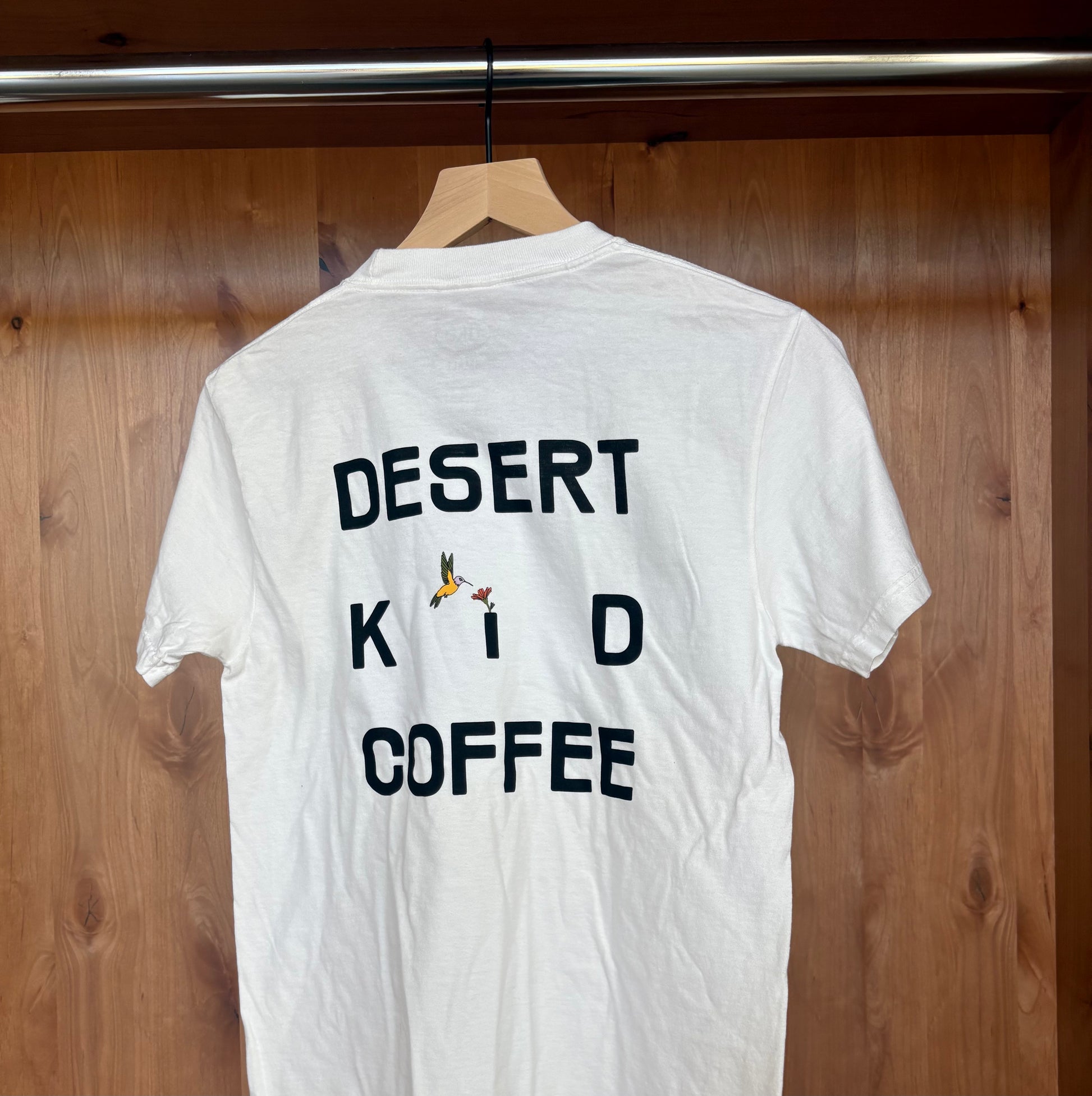 White t-shirt with 'DESERT KID COFFEE' text on a wooden background