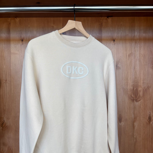 Beige sweatshirt with 'DKC' logo on a wooden background